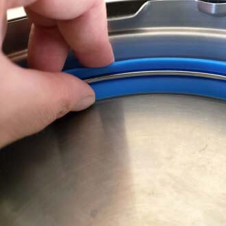 Fingers checking the placement of the seal on a pressure cooker lid