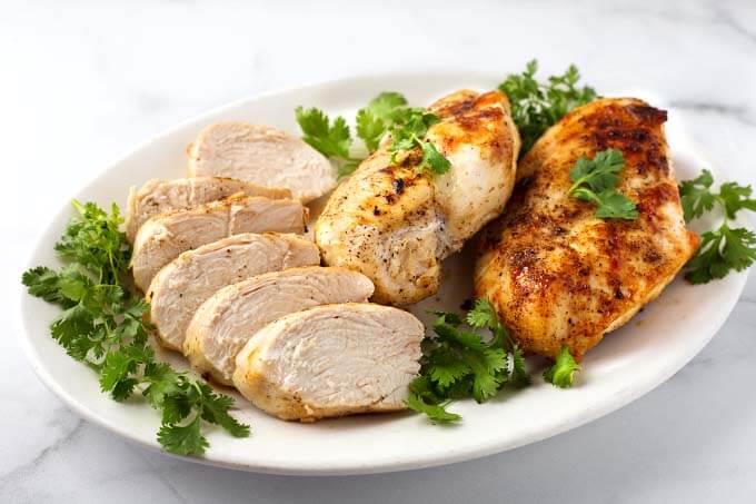 Sliced Air Fryer Chicken Breasts on white plate garnished with parsley