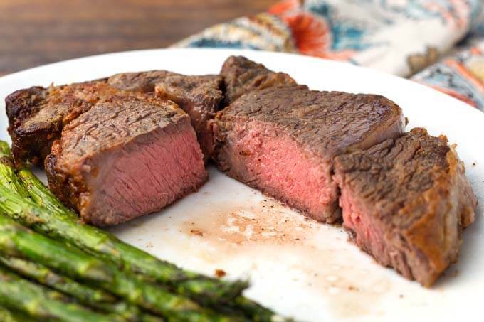 Cut Air Fryer Rib Eye Steak with asparagus on white plate