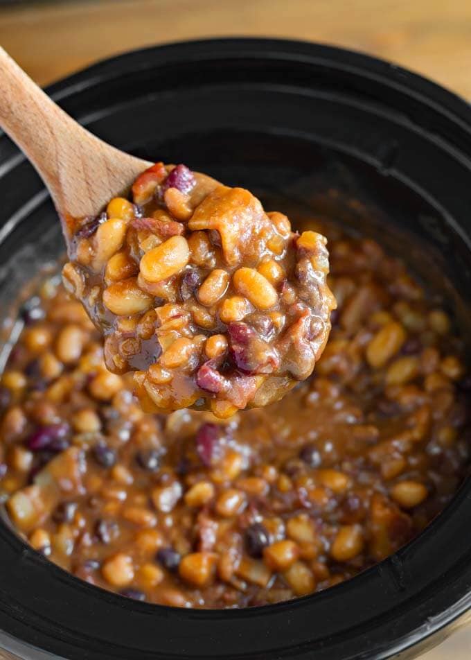 Close up of Baked Beans on wooden mixing spoon over slow cooker