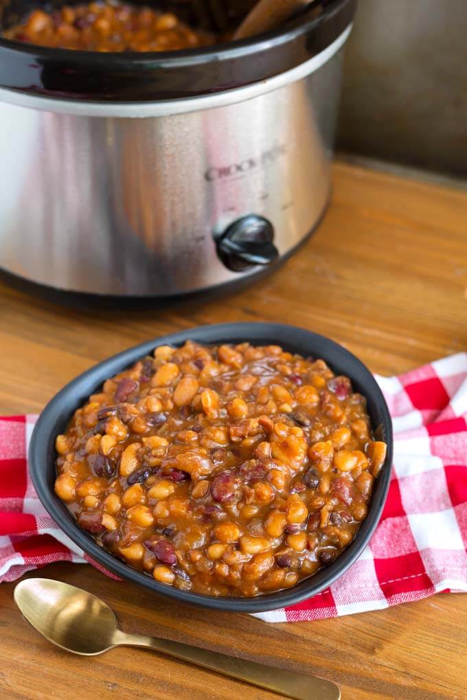 Baked Beans in black bowl on red gingham napkin in front of pressure cooker