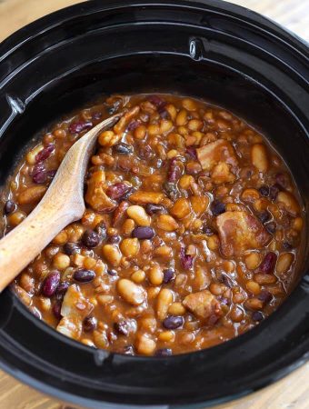 Baked Beans in a slow cooker with wooden mixing spoon