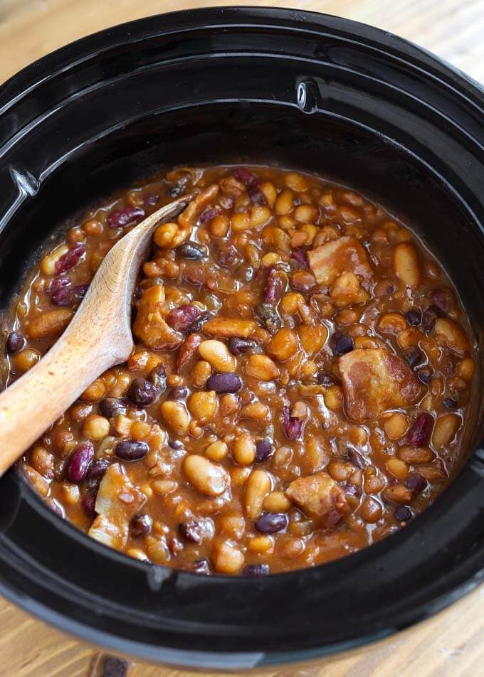 Baked Beans in a slow cooker with wooden mixing spoon