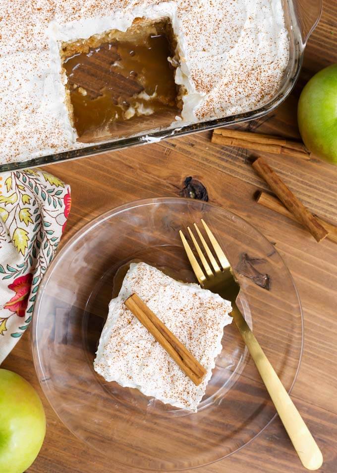 Top view of slice of Caramel Apple Poke Cake on glass plate with gold fork in front of rest of cake