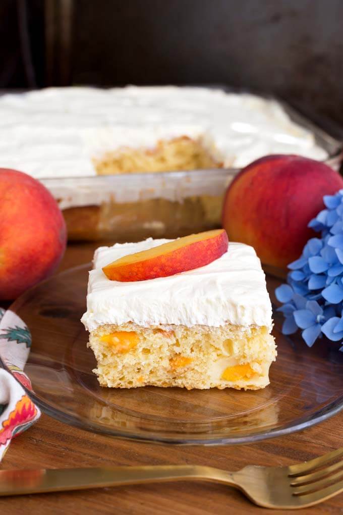 Slice of Easy Peach Potluck Cake on glass plate in front of rest of cake