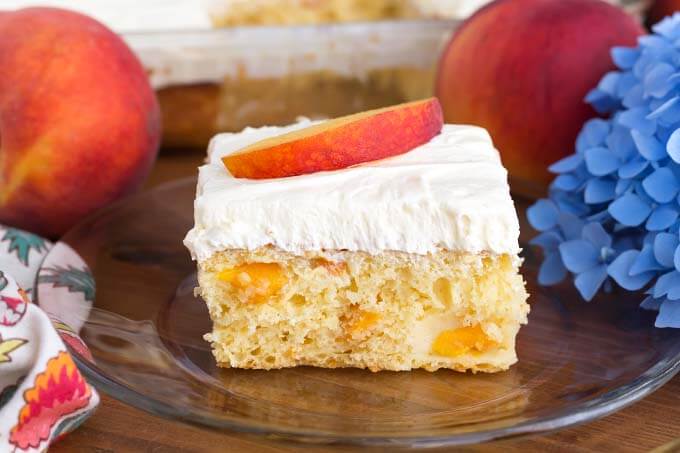 Slice of Easy Peach Potluck Cake on glass plate in front of rest of cake