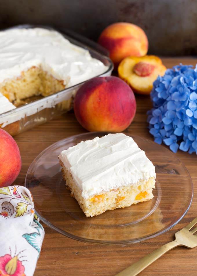 Easy Peach Potluck Cake on glass plate in front of peaches and rest of cake