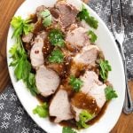 Top view of Sliced Balsamic Pork Loin Roast with fresh parsley on a white oblong platter