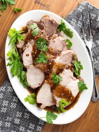 Top view of Sliced Balsamic Pork Loin Roast with fresh parsley on a white oblong platter