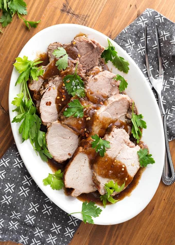 Top view of Sliced Balsamic Pork Loin Roast with fresh parsley on a white oblong platter