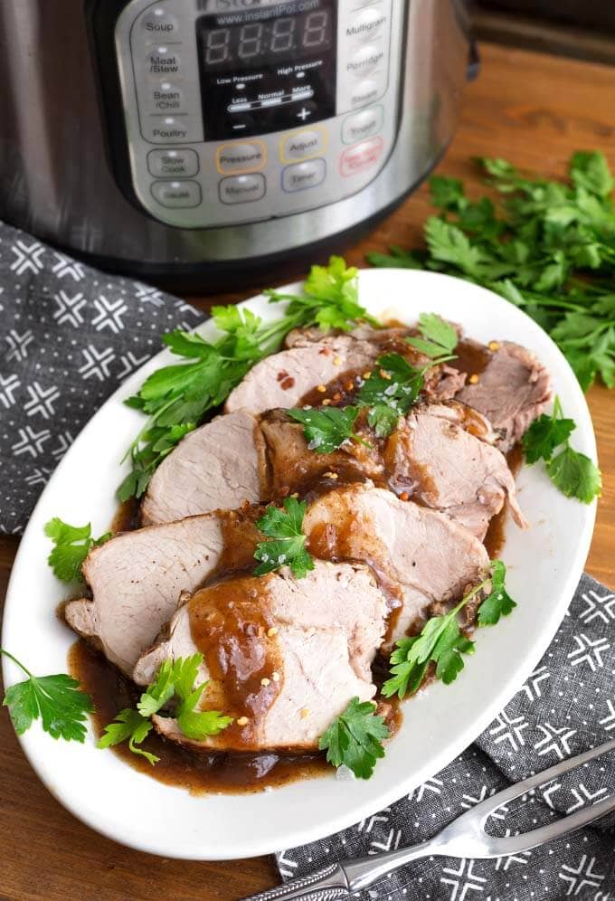 Sliced Balsamic Pork Loin Roast with fresh parsley on a white oblong platter in front of a pressure cooker