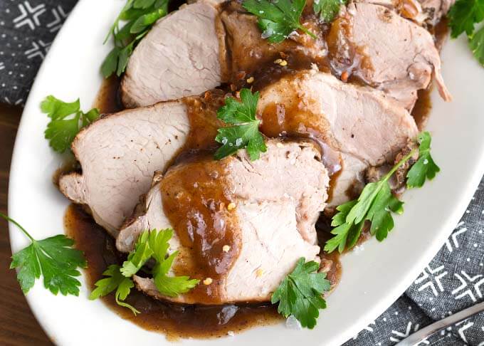 Closeup of Sliced Balsamic Pork Loin Roast with fresh parsley on a white oblong platter