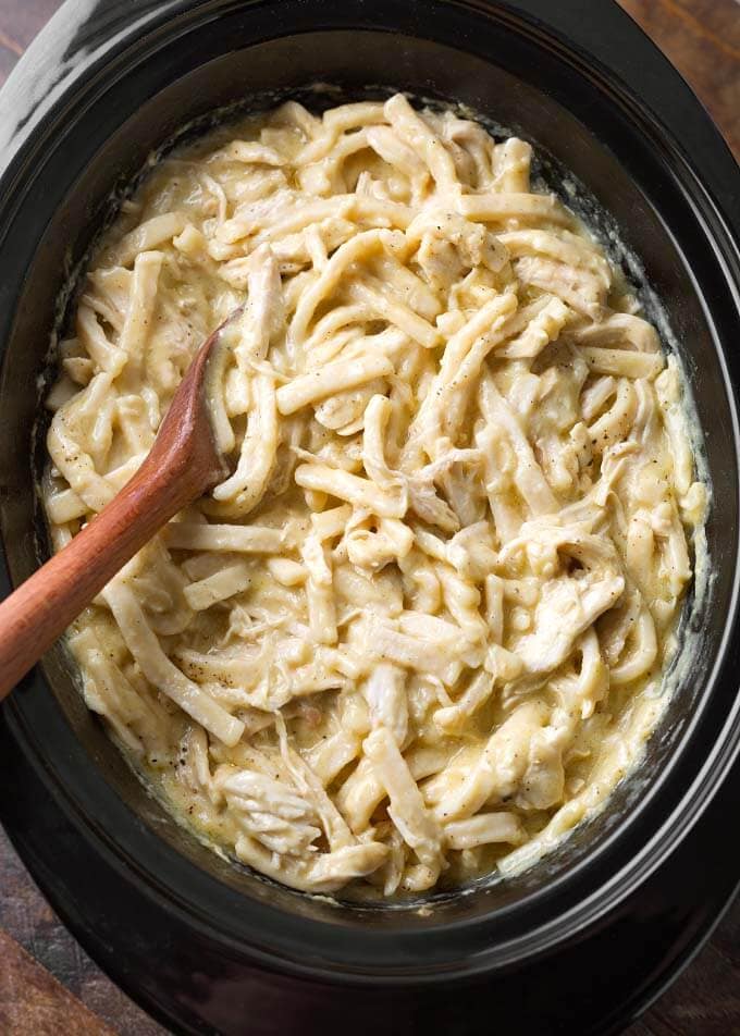 Chicken and Noodles in slow cooker with wooden mixing spoon