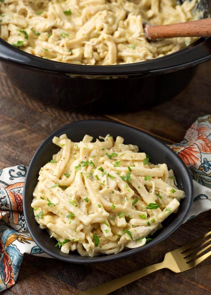 Chicken and Noodles in black bowl in front of slow cooker