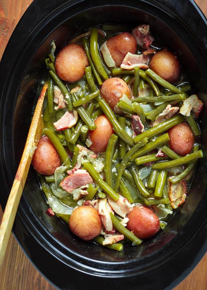 Green Beans with Bacon and Potatoes in slow cooker with wooden mixing spoon