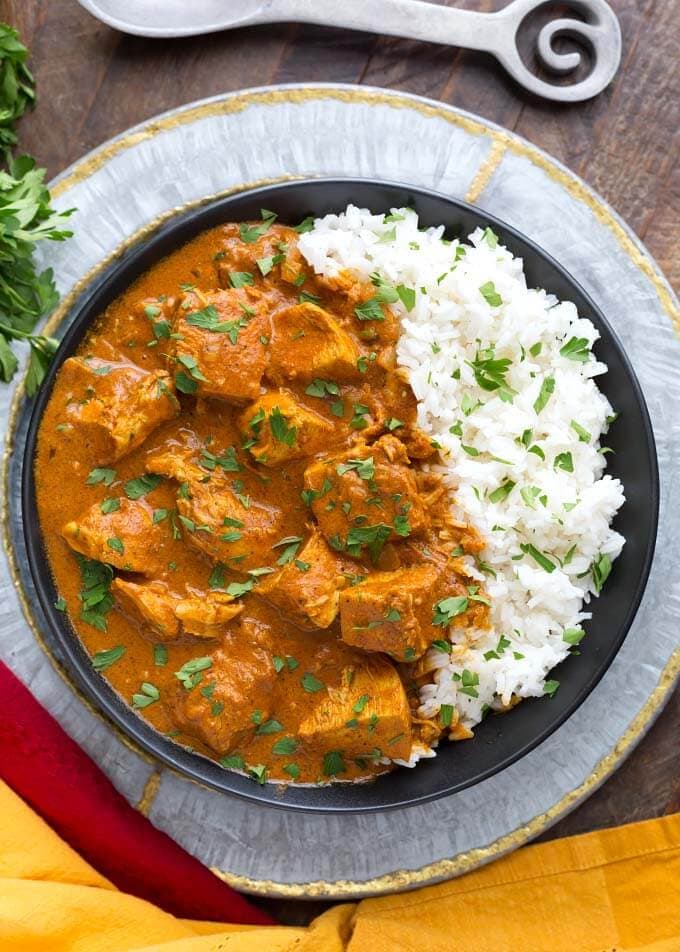 Indian Butter Chicken with white rice on a black plate on top of a silver platter