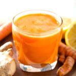 Fresh Turmeric Tonic in small glass next to fresh ginger root and turmeric