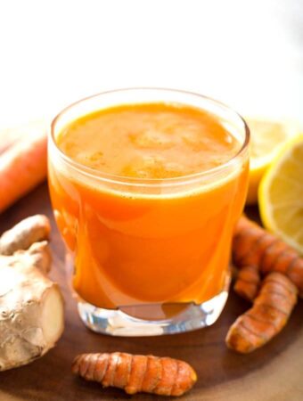 Fresh Turmeric Tonic in small glass next to fresh ginger root and turmeric