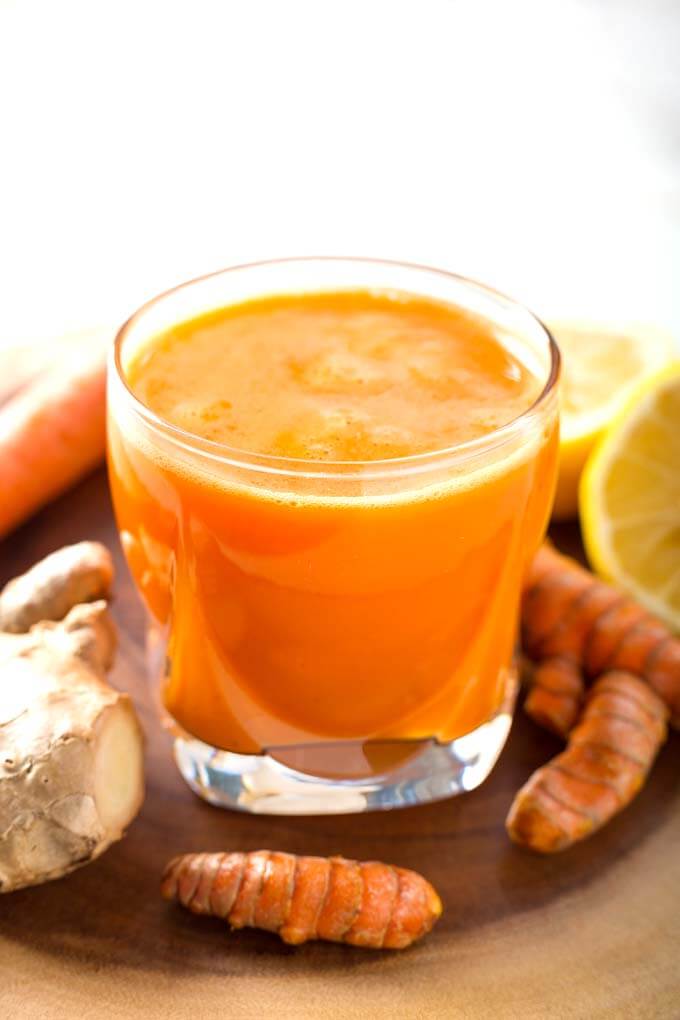 Fresh Turmeric Tonic in small glass next to fresh ginger root and turmeric