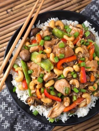 Cashew Chicken over rice on black plate with wooden chopsticks