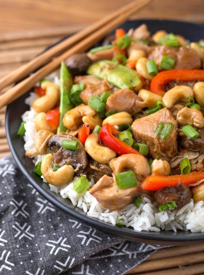 Close up of Cashew Chicken over rice on black plate with wooden chopsticks