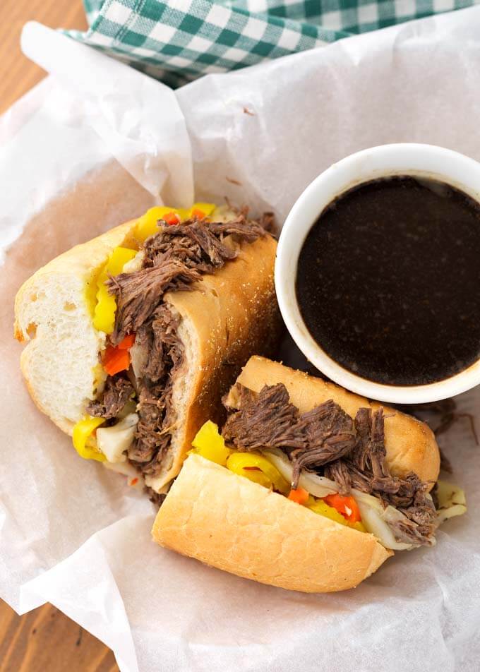Italian Beef sandwich cut in half next to small bowl of sauce in white paper-lined basket
