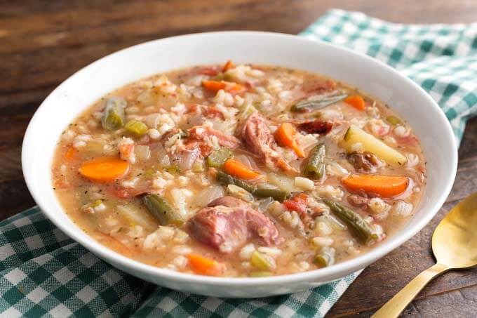 Slow Cooker Ham Vegetable Barley Soup in white bowl on green gingham napkin