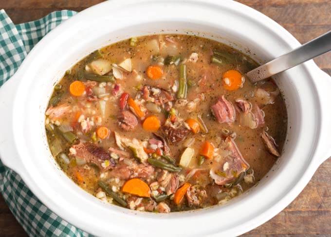 Ham Vegetable Barley Soup in white slow cooker with ladle