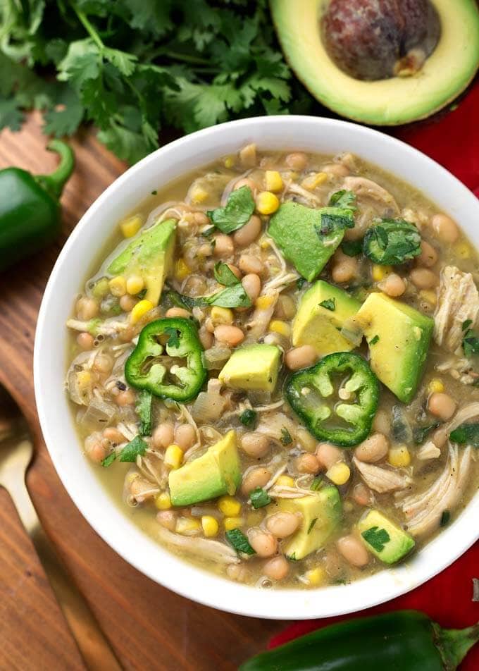 White Chicken Chili topped with diced avocado and fresh jalapeno slices in a white bowl on a wooden board