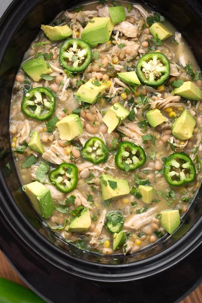 Closeup of White Chicken Chili topped with diced avocado and fresh jalapeno slices in a black slow cooker