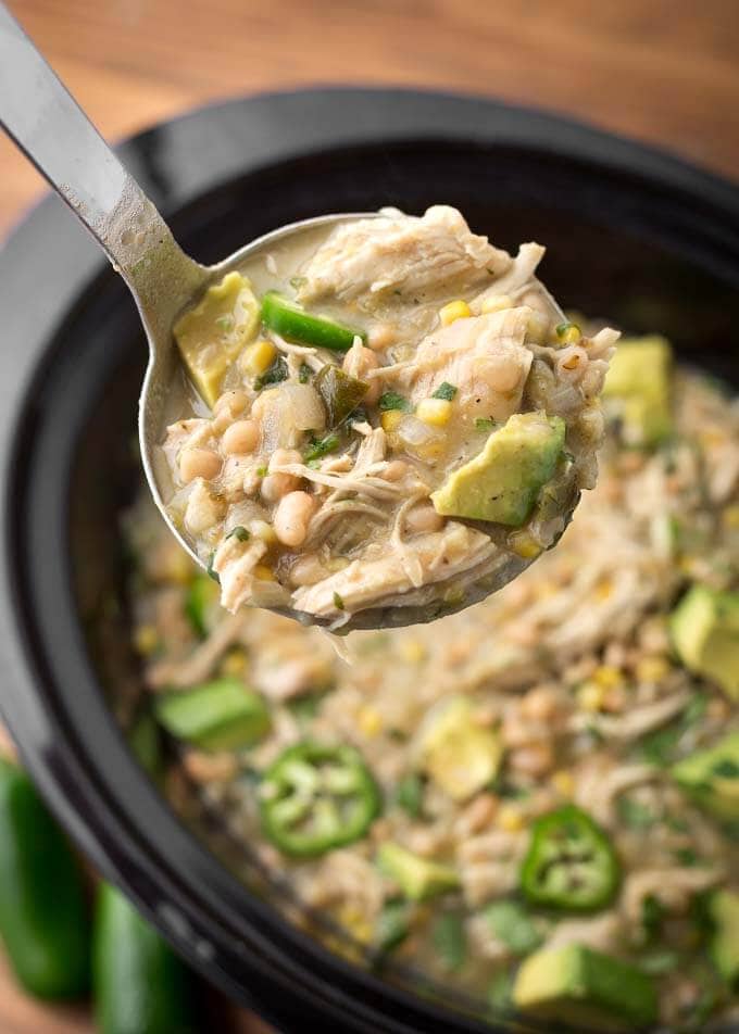 Closeup of ladle full of White Chicken Chili over black slow cooker of chili