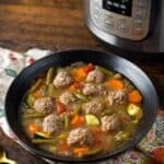 Pressure Cooker Albondigas Soup in black bowl in front of pressure cooker