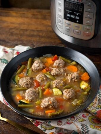 Pressure Cooker Albondigas Soup in black bowl in front of pressure cooker