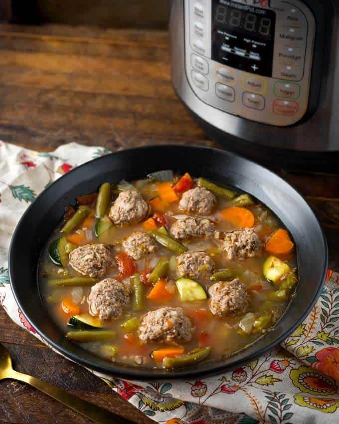 Pressure Cooker Albondigas Soup in black bowl in front of pressure cooker