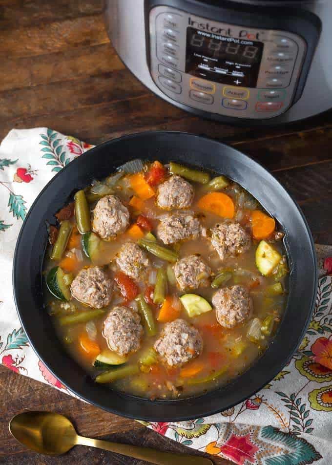 Pressure Cooker Albondigas Soup in black bowl in front of pressure cooker