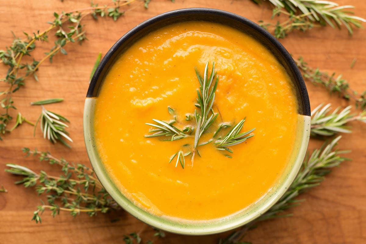 Instant Pot Butternut Squash Soup in a white bowl surrounded by rosemary