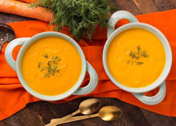 Two light blue bowls of Pressure Cooker Carrot Soup on orange background