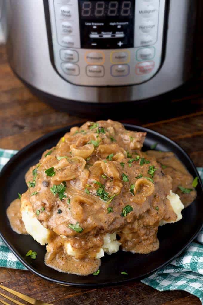 Pressure Cooker Cube Steak with Onion Gravy on black plate in front of Pressure Cooker