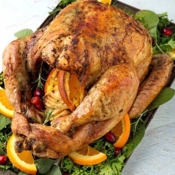 Thanksgiving Turkey on baking sheet with vegetables, herbs, sliced oranges and cranberries