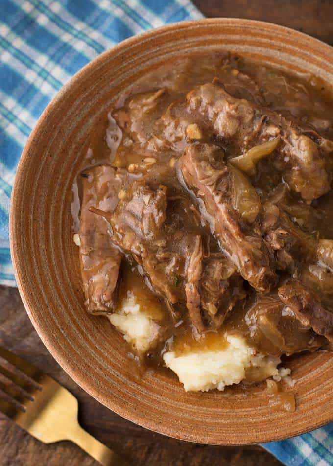 Pressure Cooker French Onion Pot Roast over mashed potatoes in brown bowl next to gold fork