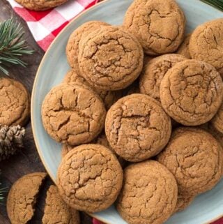 Several Soft Chewy Ginger Cookies on grey plate with red gingham napkin and pine needles in background