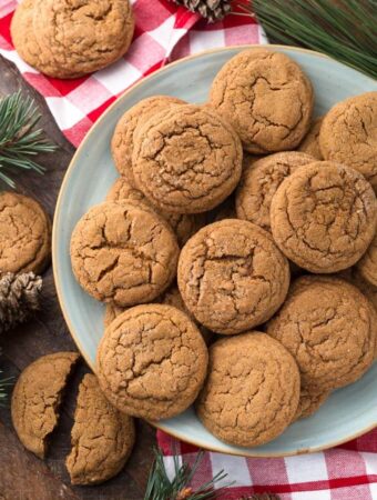 Several Soft Chewy Ginger Cookies on grey plate with red gingham napkin and pine needles in background