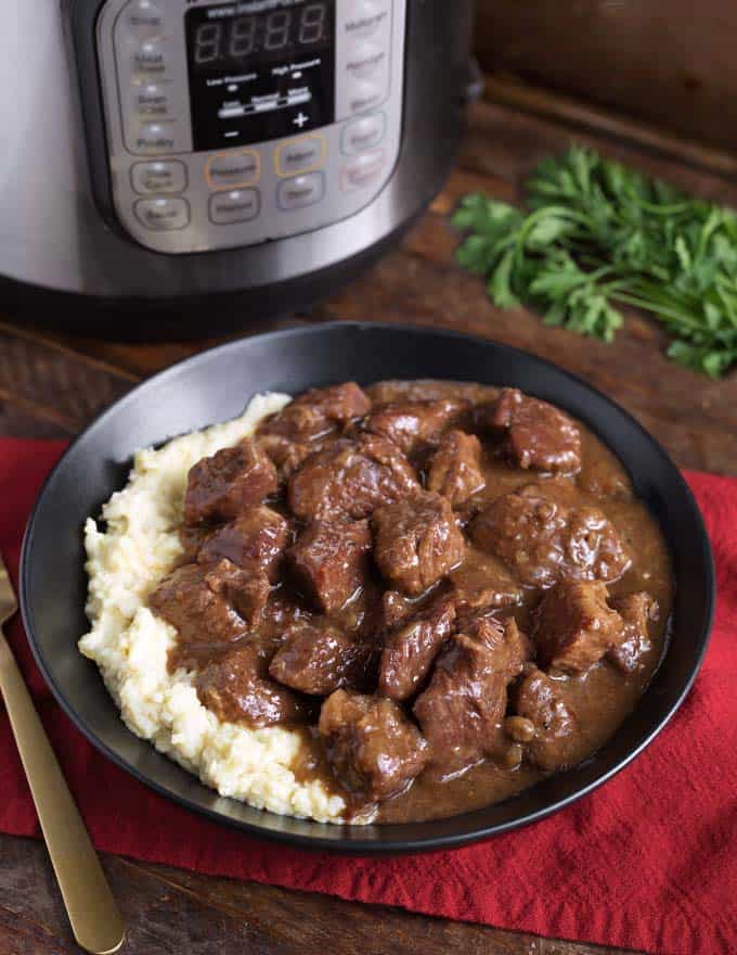 Instant Pot Beef Tips and mashed potatoes in a black bowl in front of pressure cooker