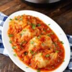 Pressure Cooker Stuffed Cabbage Rolls on white oval plate in front of pressure cooker