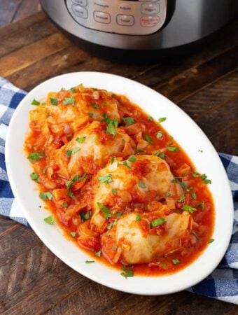 Pressure Cooker Stuffed Cabbage Rolls on white oval plate in front of pressure cooker