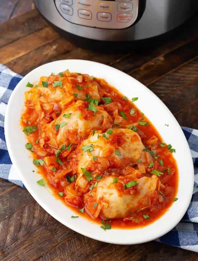 Pressure Cooker Stuffed Cabbage Rolls on white oval plate in front of pressure cooker