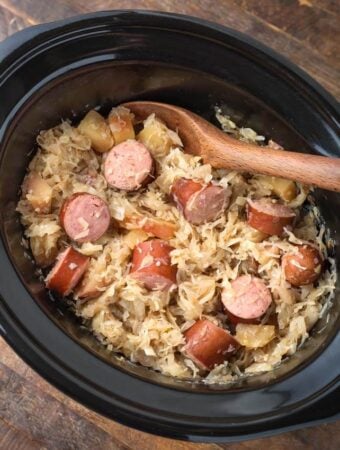 Slow Cooker Sauerkraut and Kielbasa with wooden mixing spoon