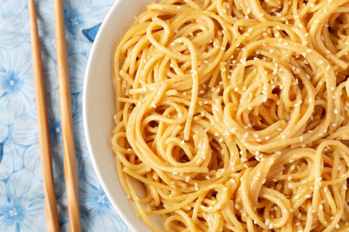 close up of Garlic Noodles in white bowl next to wooden chopsticks