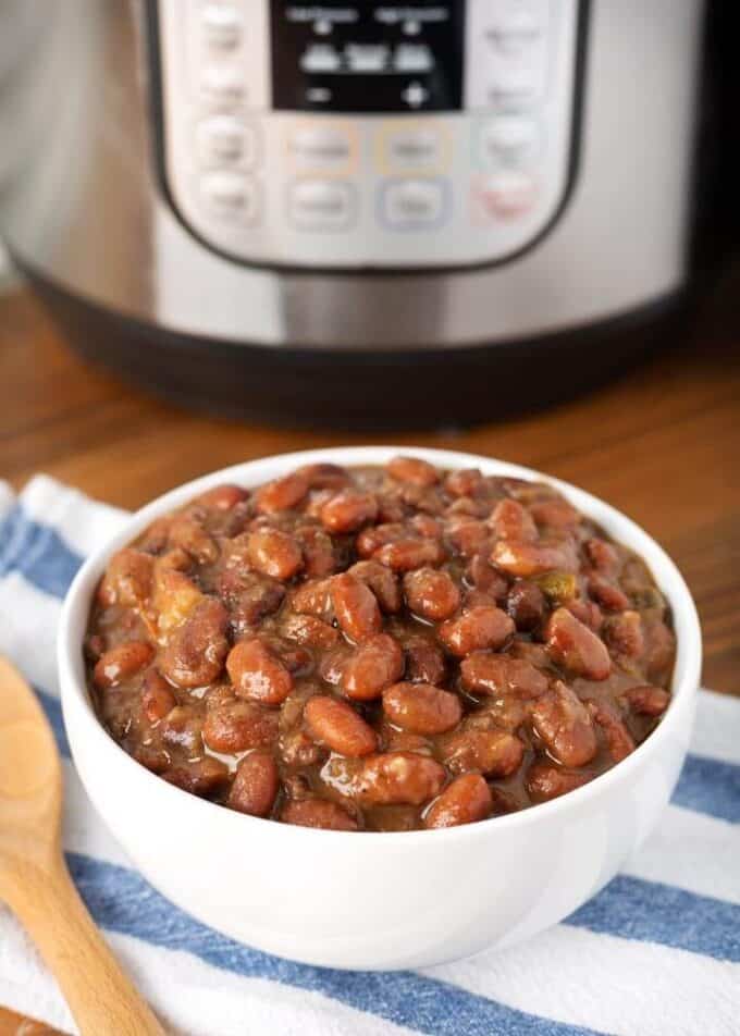 Pressure cooker Mexican Pinto Beansin white bowl in front of pressure cooker