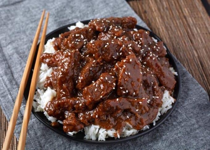 Pressure cooker Mongolian Beef over white rice on black plate with wooden chopsticks